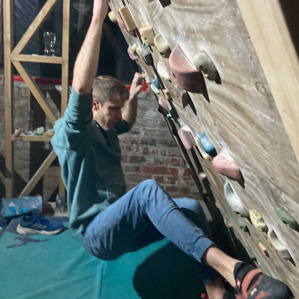 Person climbing a rock wall indoors with a green mat below