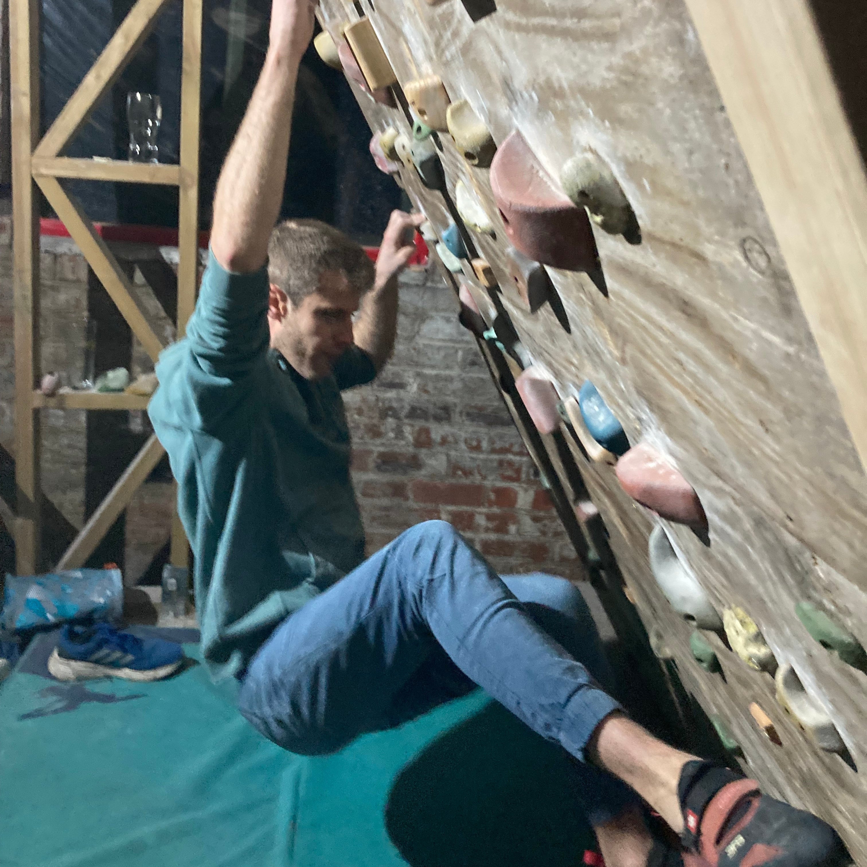 Person climbing a rock wall indoors with a green mat below