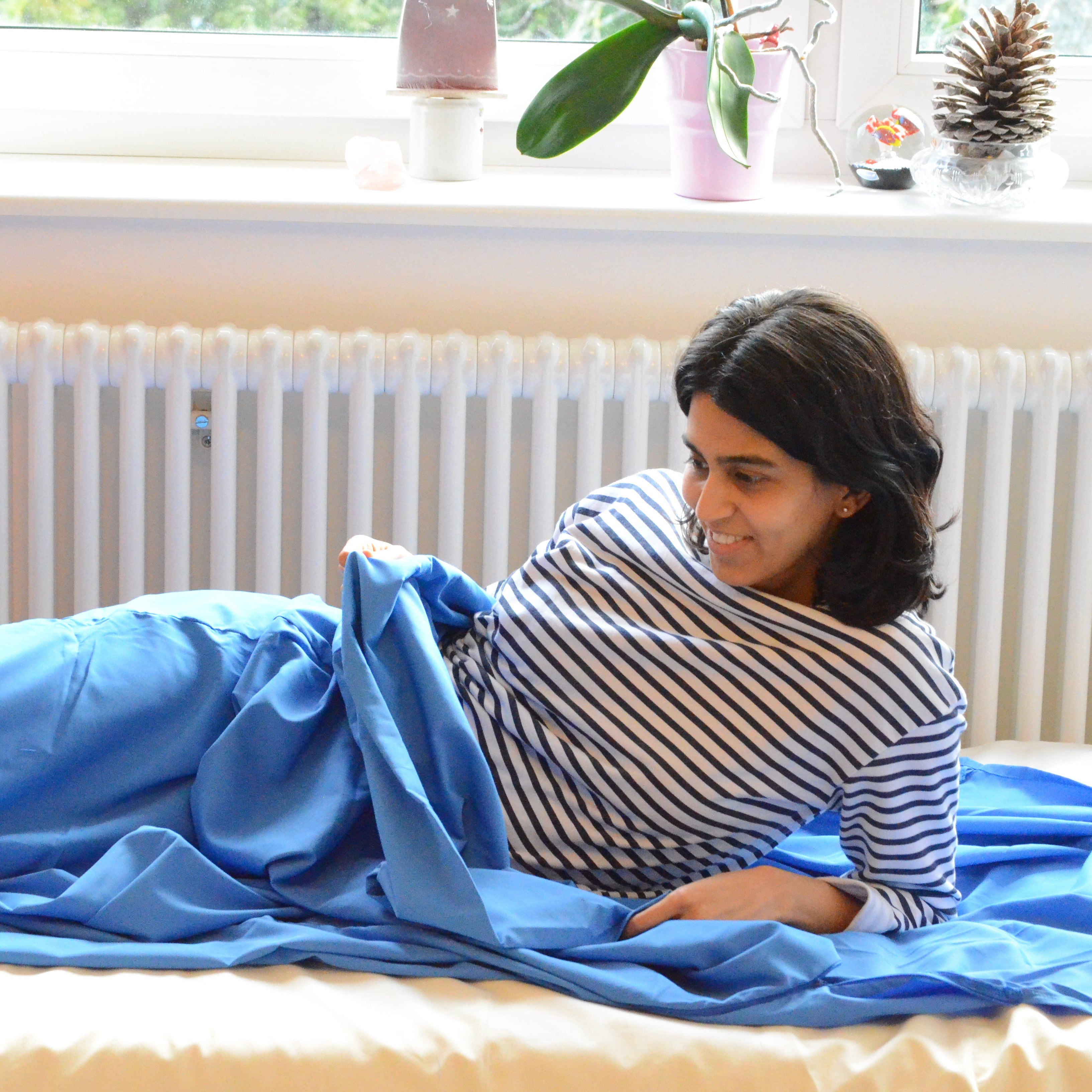 Woman lying in a blue sleeping liner in a room with a window and radiator.