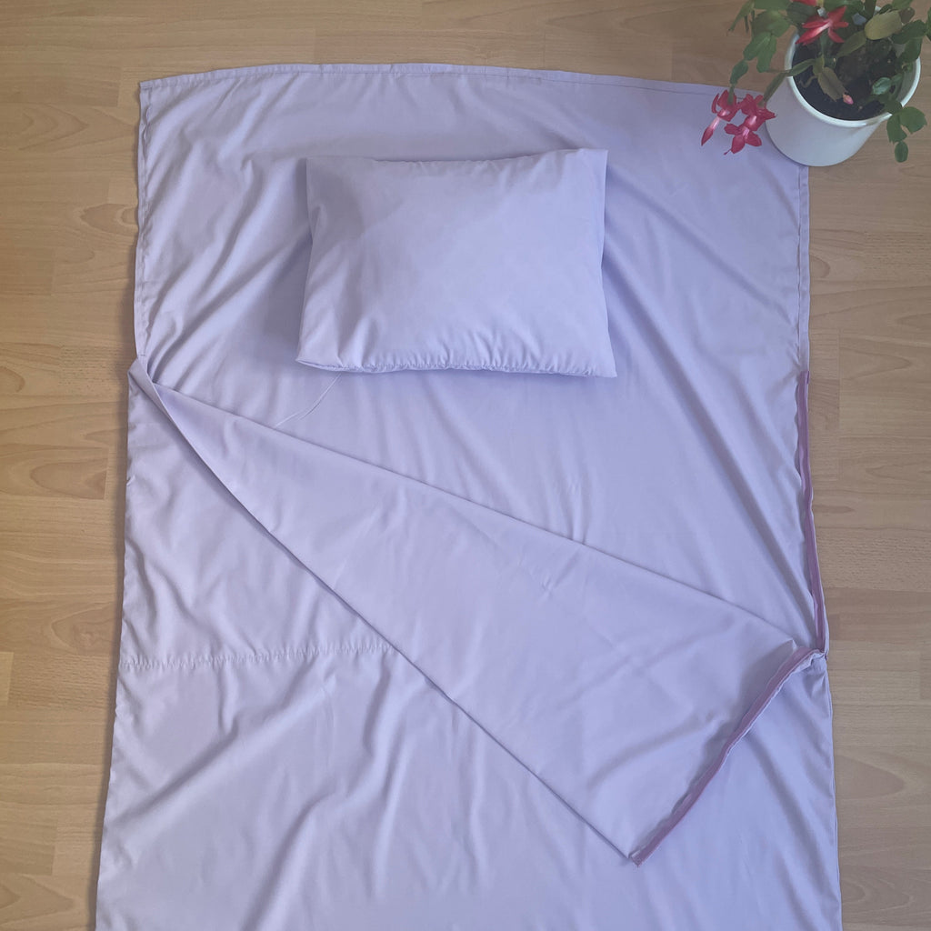 Purple bedspread with a pillow on a wooden floor next to a potted plant.