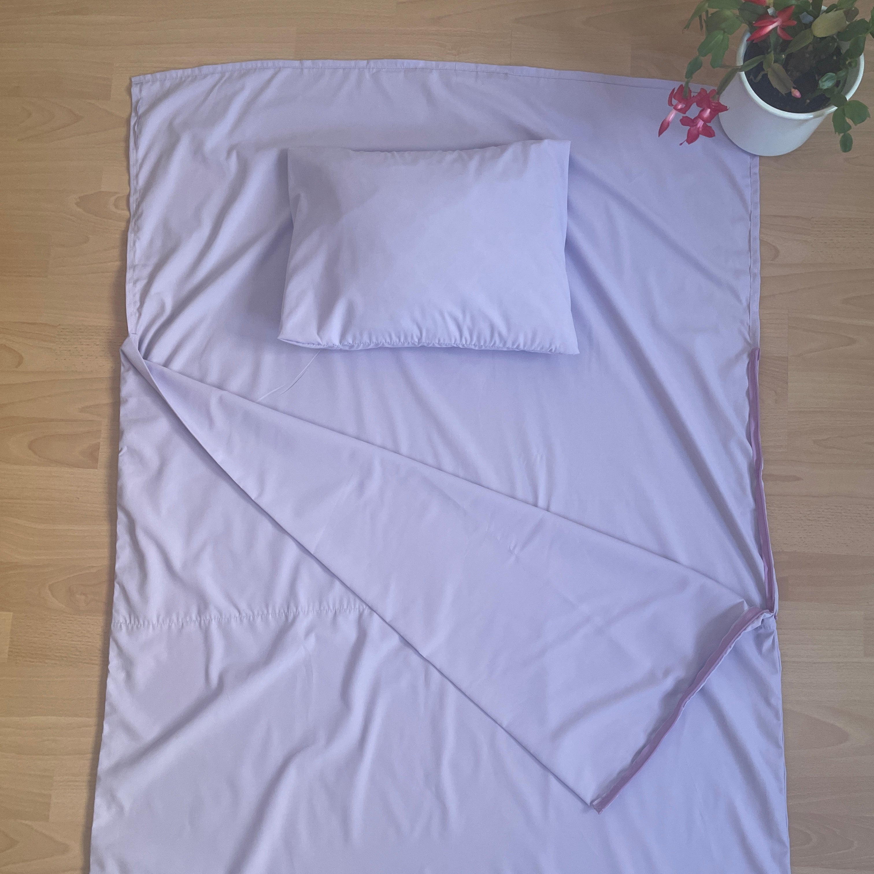 Purple bedspread with a pillow on a wooden floor next to a potted plant.
